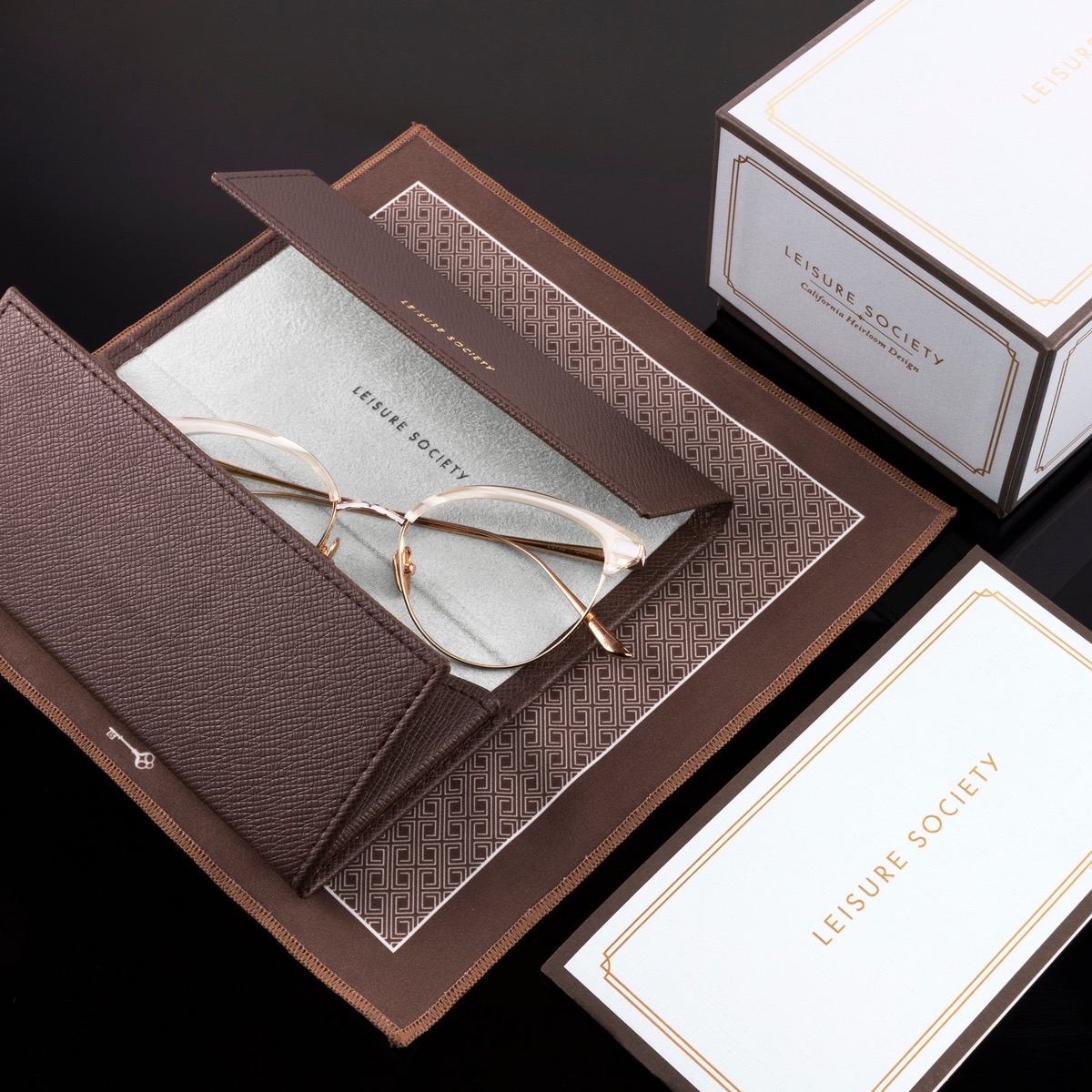 Optical frame with transition lenses, open in its case with packaging box and authenticity card on black